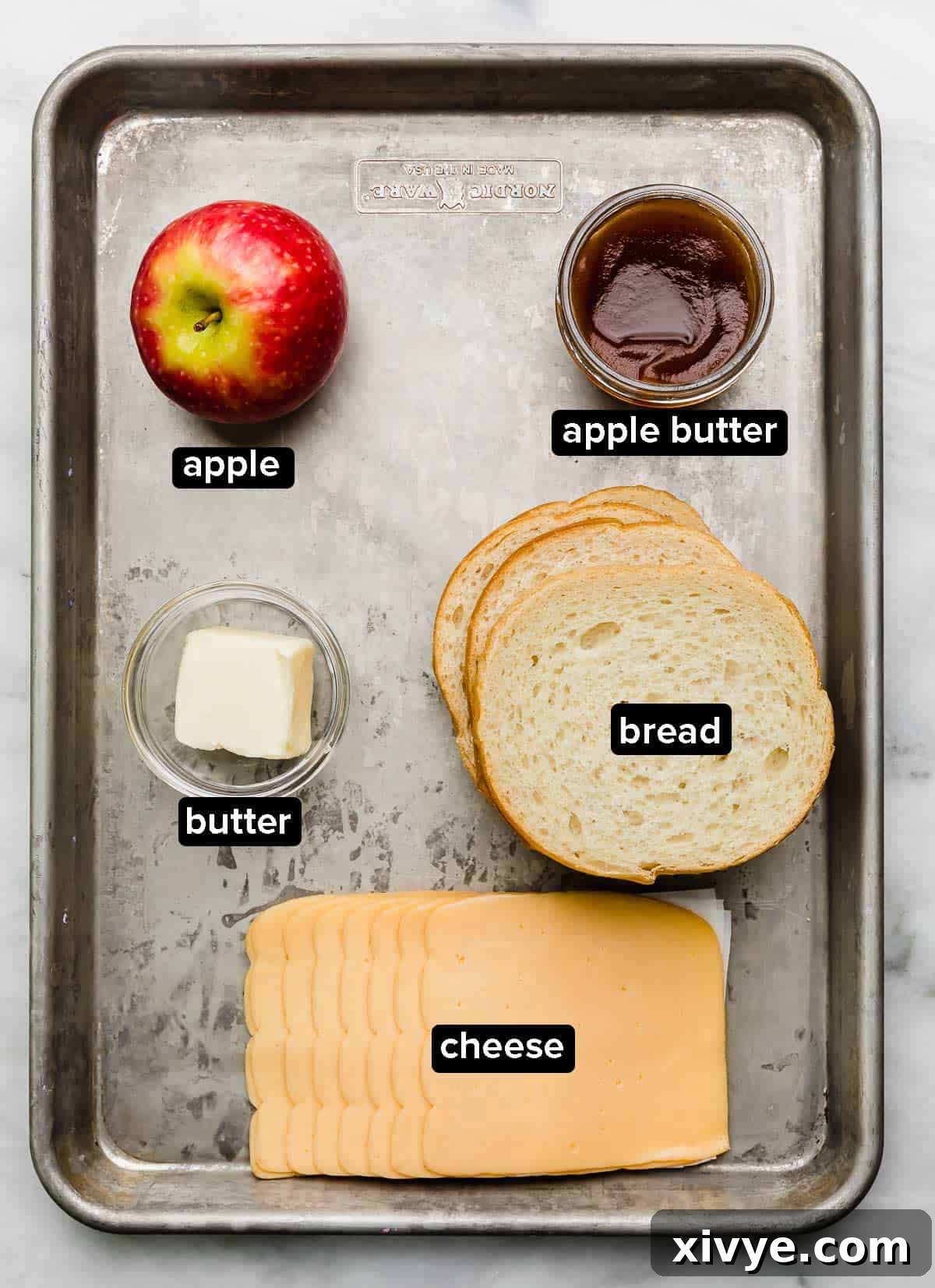 Crispy Apple Cheese Melt 3 Apple Grilled Cheese Sandwich ingredients on a silver baking sheet: fresh apple, apple butter, cheese, bread, and butter.
