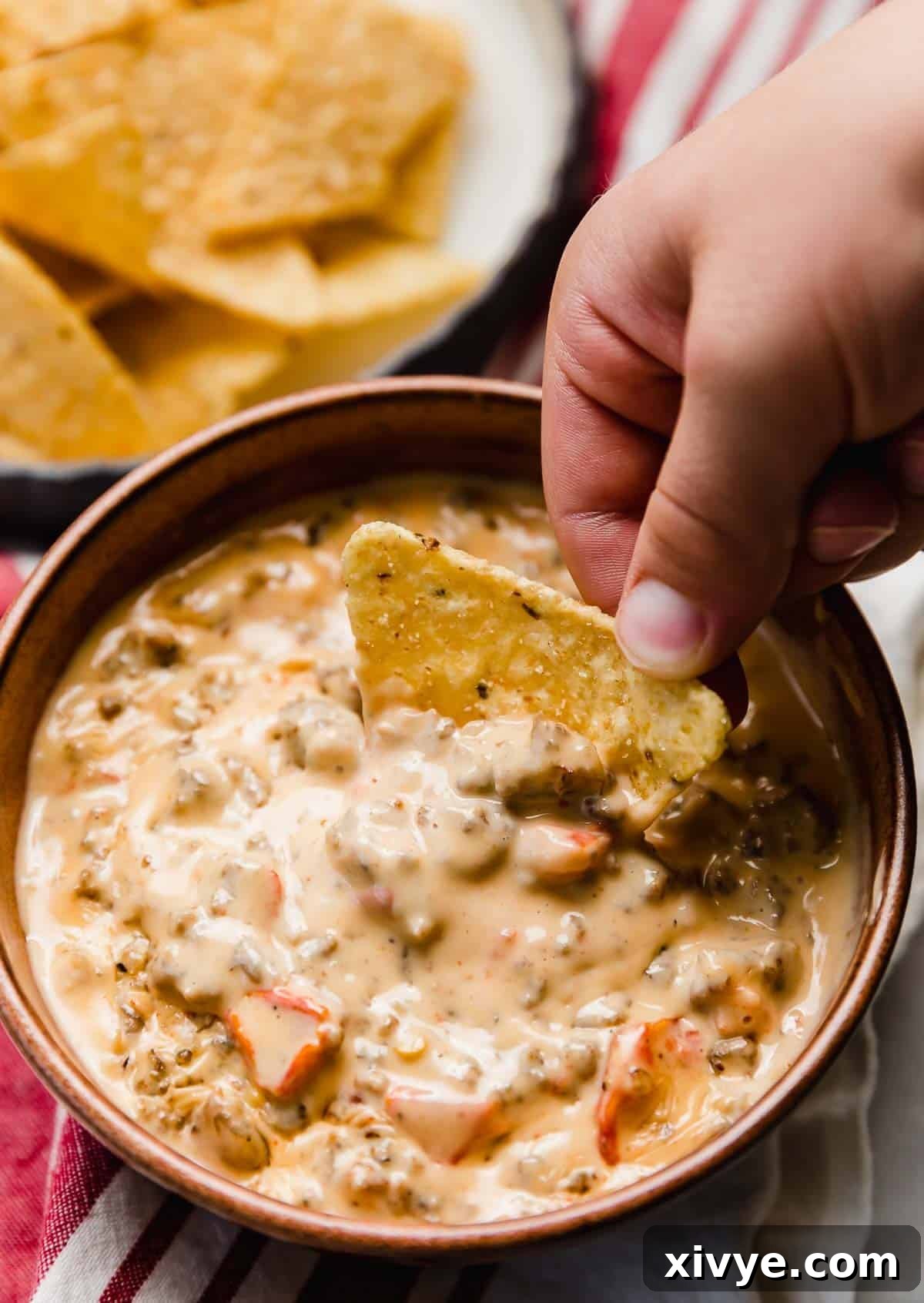 Kickin' Cream Cheese Sausage Dip 5 Cream Cheese Sausage Rotel Dip made in a crock pot, with a hand scooping a tortilla chip into the Rotel dip.
