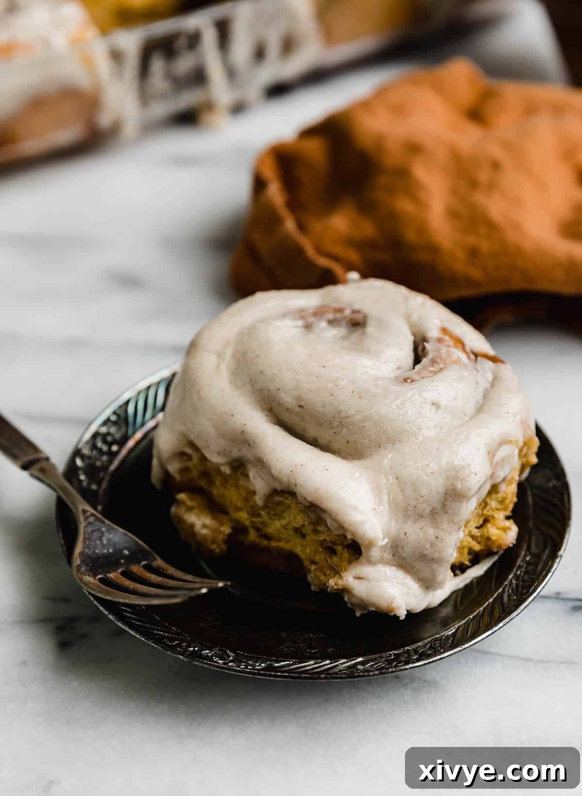 Warm Autumn Pumpkin Scrolls 45 A perfectly glazed pumpkin cinnamon roll resting on a sleek black plate, set against a pristine white marble background, ready to be enjoyed.