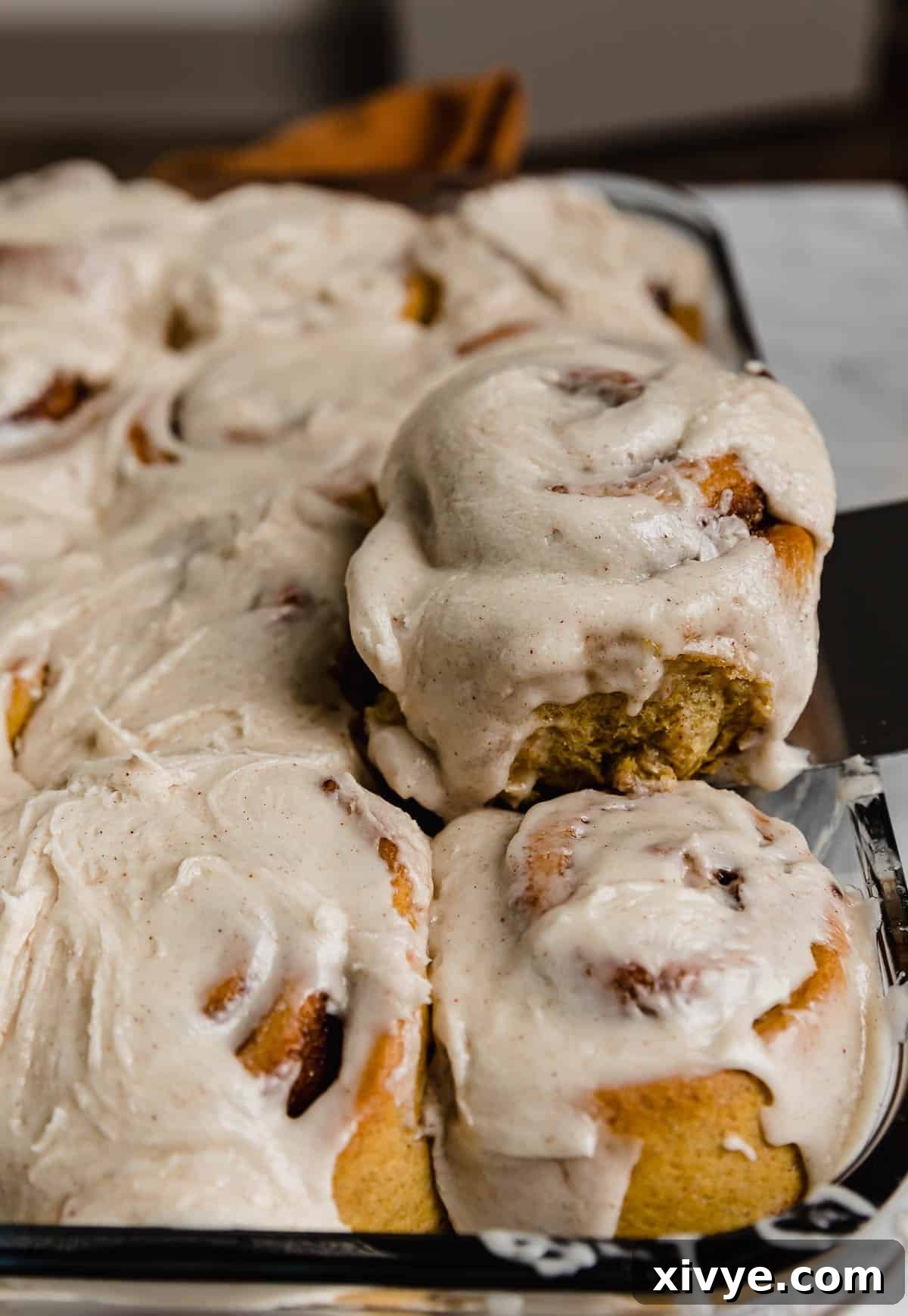 Warm Autumn Pumpkin Scrolls 8 Close-up shot of decadent Pumpkin Cinnamon Rolls, generously topped with a rich cinnamon icing, ready to be served.