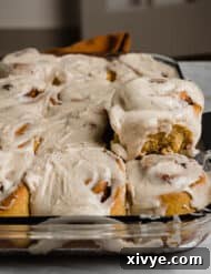 Warm Autumn Pumpkin Scrolls 9 A rectangle baking dish loaded with soft pumpkin cinnamon rolls, with a metal spatula picking up one of the cinnamon rolls, ready to be served.