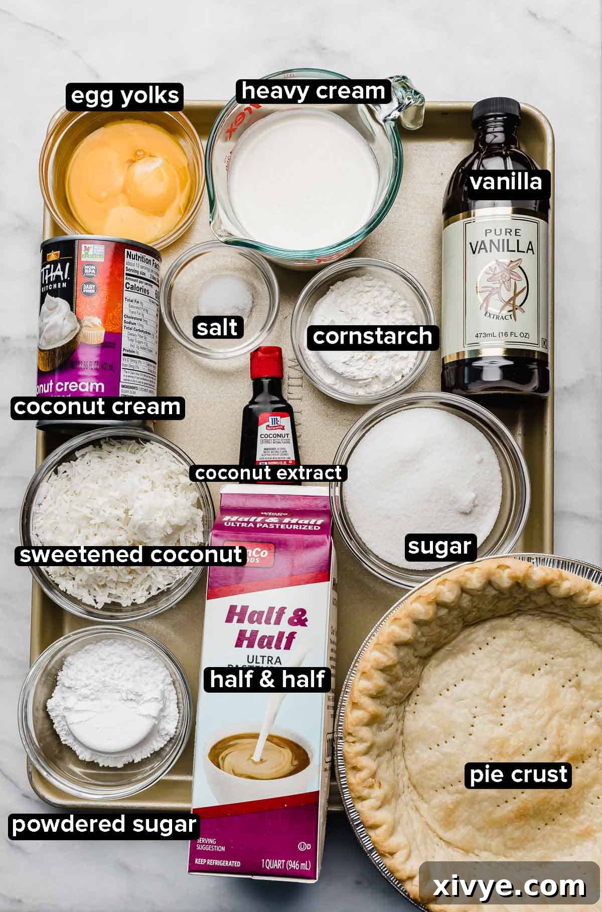 Creamy Coconut Bliss 3 A beautifully arranged baking sheet featuring all the fresh and quality ingredients required for making a homemade Coconut Cream Pie: a pre-baked butter pie crust, half and half, a bowl of shredded coconut, egg yolks, granulated sugar, a can of coconut cream, a bottle of coconut extract, and sugar.