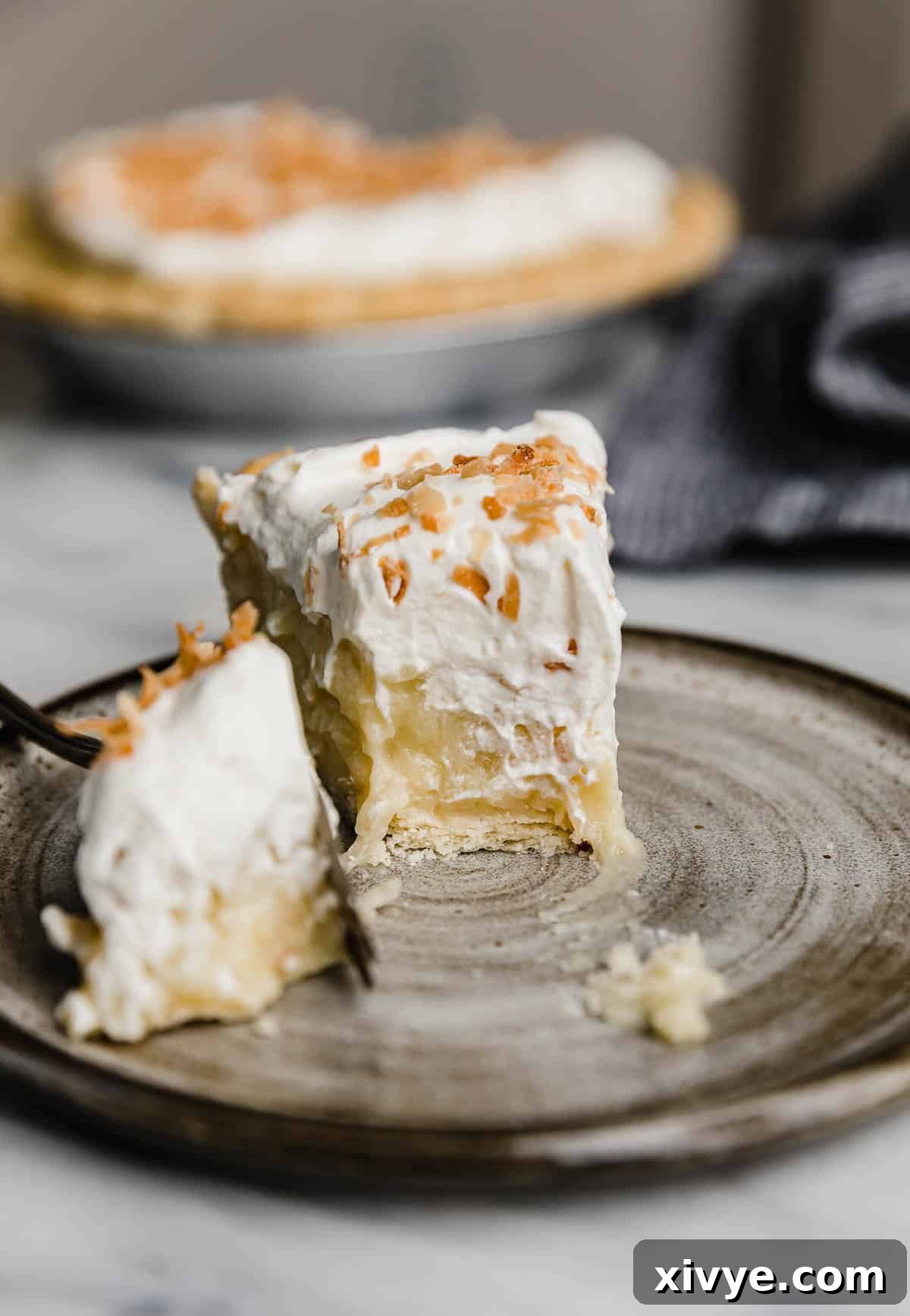Creamy Coconut Bliss 6 A perfectly portioned slice of coconut cream pie, topped generously with whipped cream and toasted coconut, with a small bite removed from the main slice, hinting at its deliciousness.