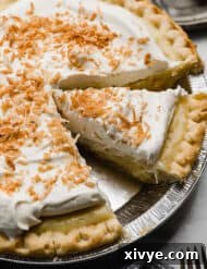A slice of coconut cream pie, topped with toasted coconut in a pie plate.
