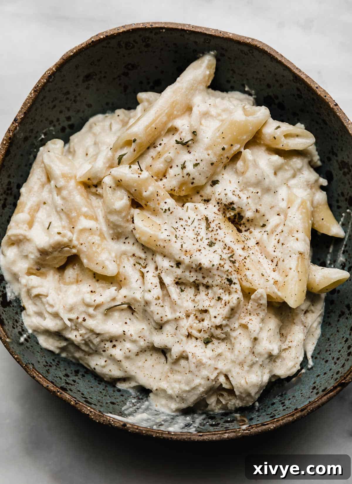A bowl of creamy chicken Alfredo pasta made with penne pasta in a blue bowl.