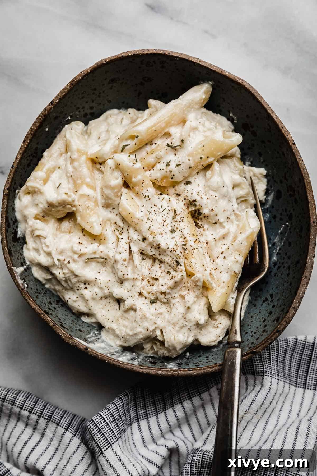 A blue bowl filled with chicken Alfredo made in a crock pot on a white marble background.