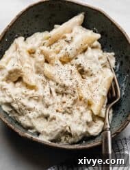 A bowl of creamy chicken Alfredo made tin penne noodles in a bowl on a white marble surface.