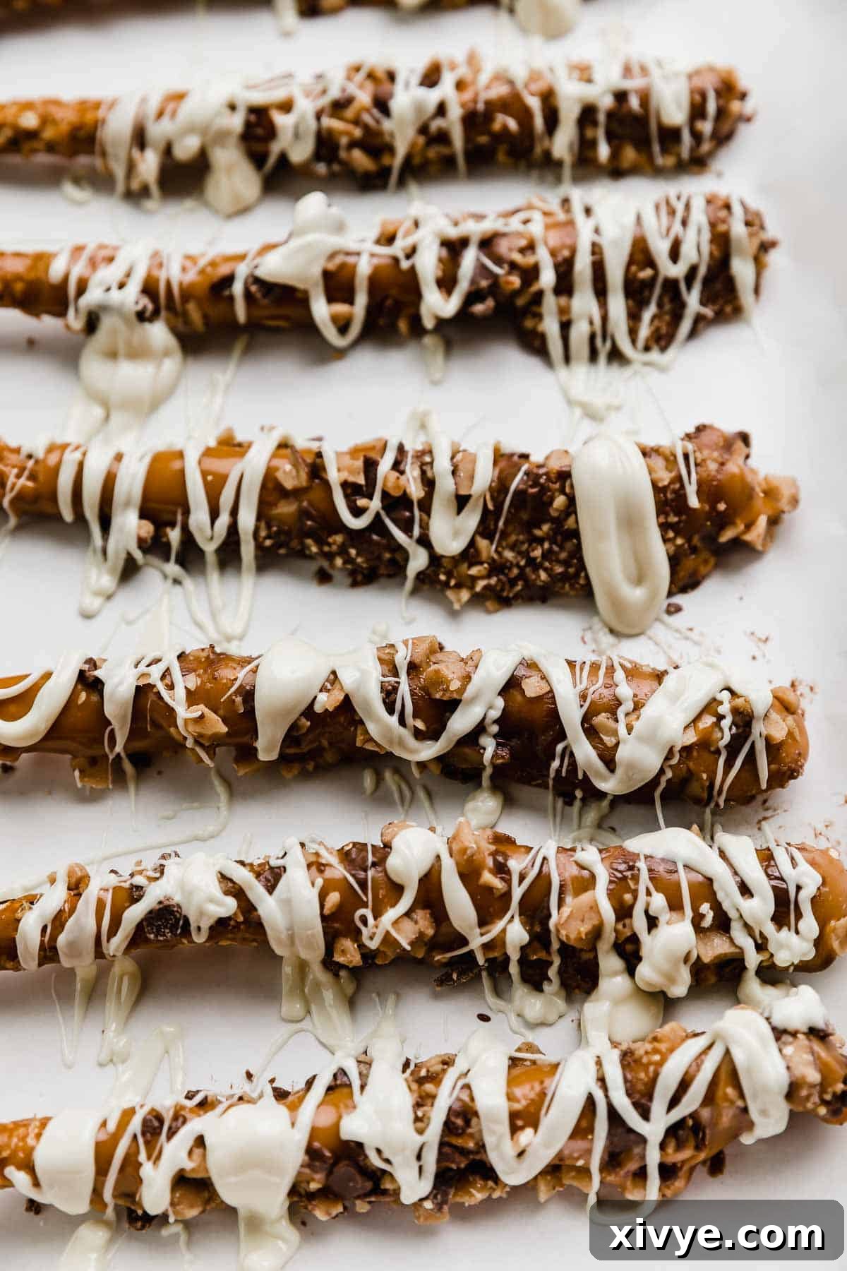 Caramel pretzels dipped in toffee bits and drizzled with white chocolate, presented beautifully on a platter.