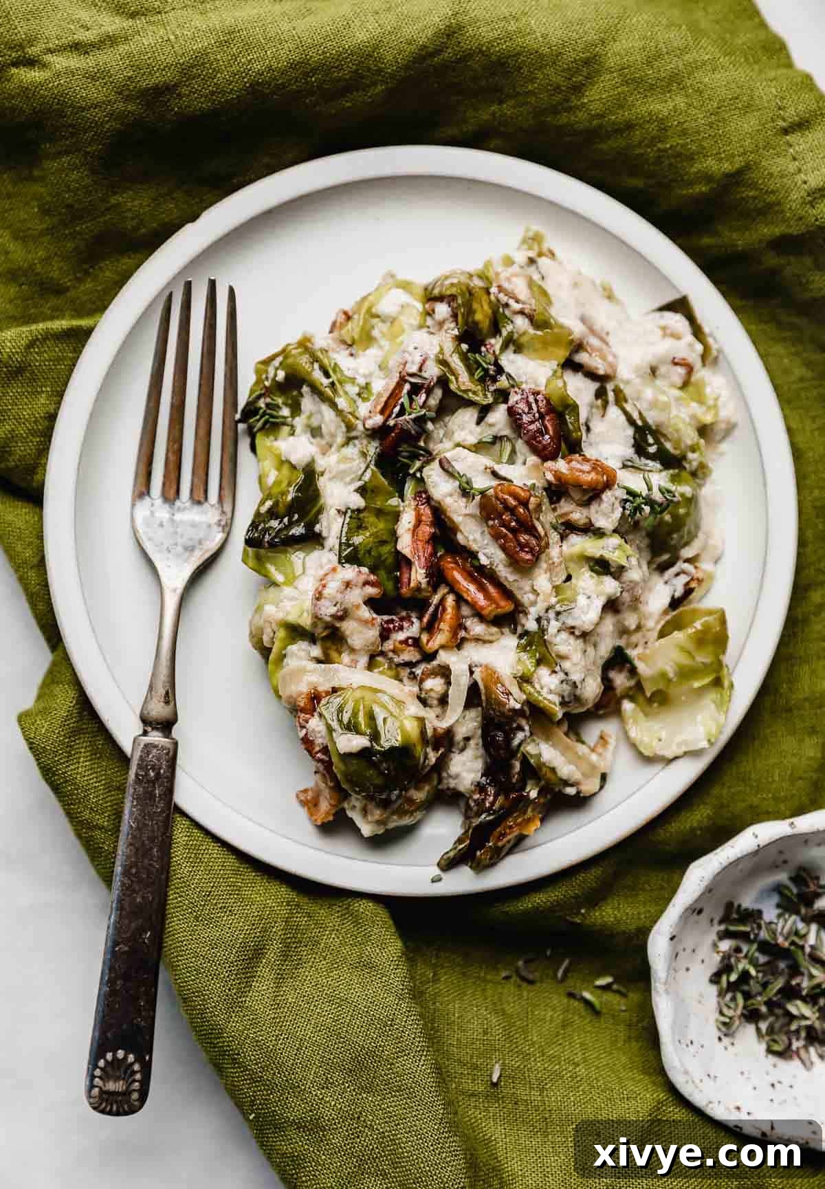 Bacon brussels sprouts gratin with pecans and gruyere cheese in a cream mixture, on a white plate resting on a green linen napkin.
