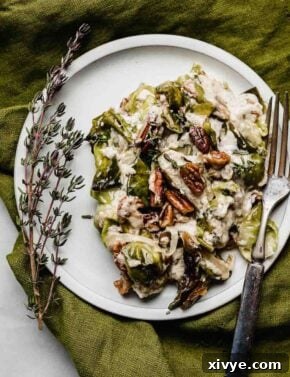 Creamy Brussels Sprouts Gratin with Bacon, pecans, and gruyere on a white plate with a fresh twig of thyme to the side of the plate.