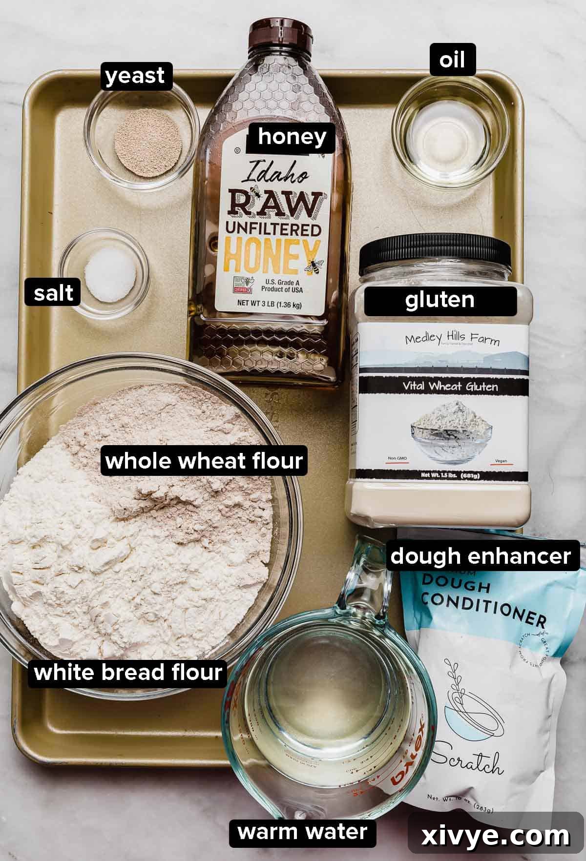 Fifty-Fifty White and Whole Wheat Bread 3 50/50 Bread recipe ingredients on a gold baking sheet (gluten, dough conditioner, yeast, salt, whole wheat flour, bread flour, yeast, oil, and honey).