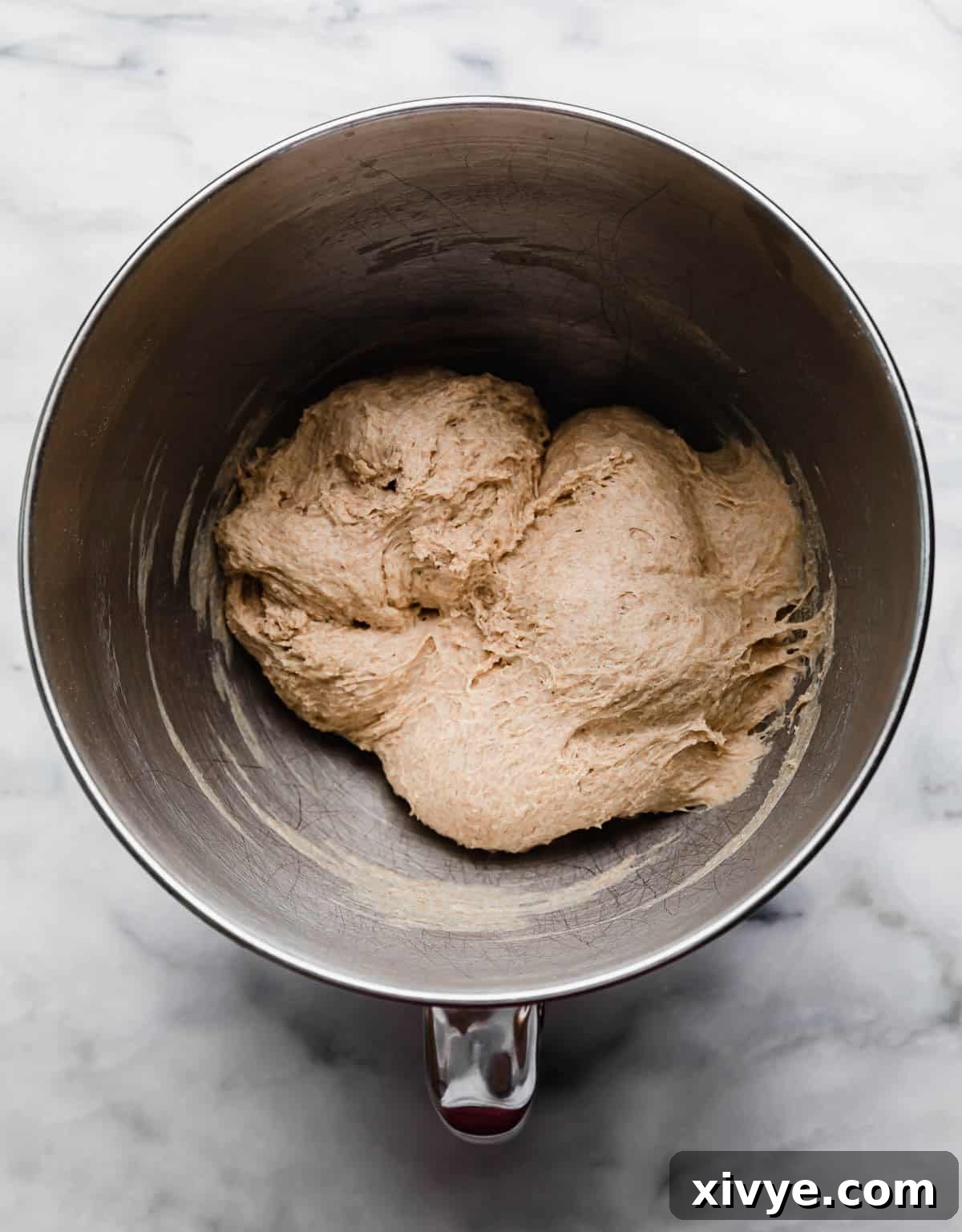Fifty-Fifty White and Whole Wheat Bread 7 50/50 bread recipe dough in a silver mixing bowl on a white marble surface.