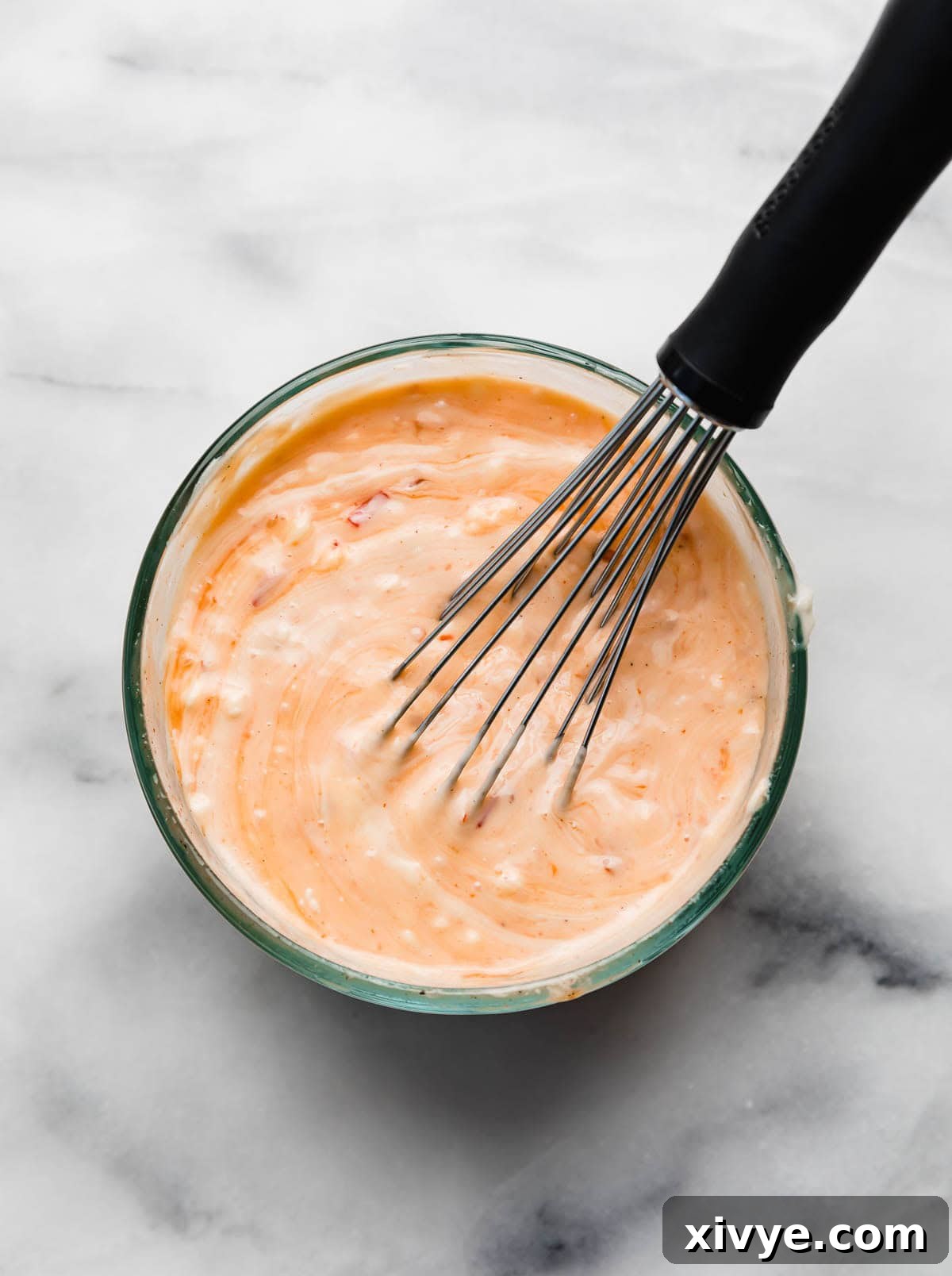 Glass bowl filled with creamy bang bang sauce and a whisk.