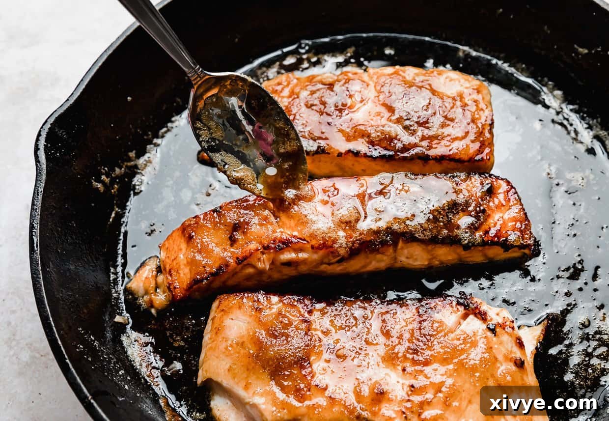 A spoon drizzling rich brown sugar glaze overtop of salmon in a black skillet. 