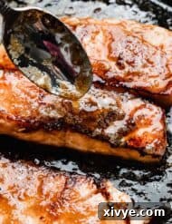 A spoon drizzling brown sugar and butter glaze overtop of a seared salmon filet.