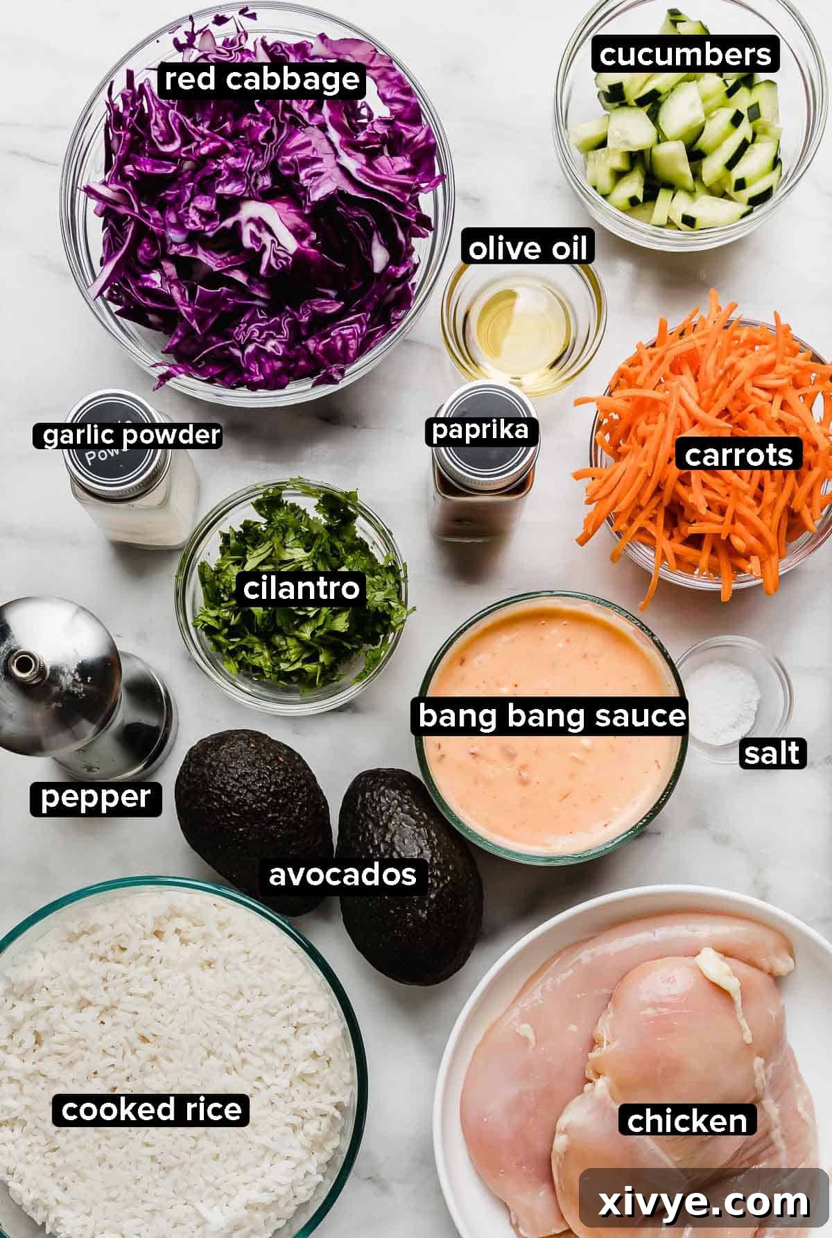 Effortless Bang Bang Chicken Bowls 3 Ingredients used to make bang bang chicken bowls on a white surface, each ingredient in a separate glass bowl: chicken, bang bang sauce, carrots, cilantro, cucumber, cabbage, seasonings.