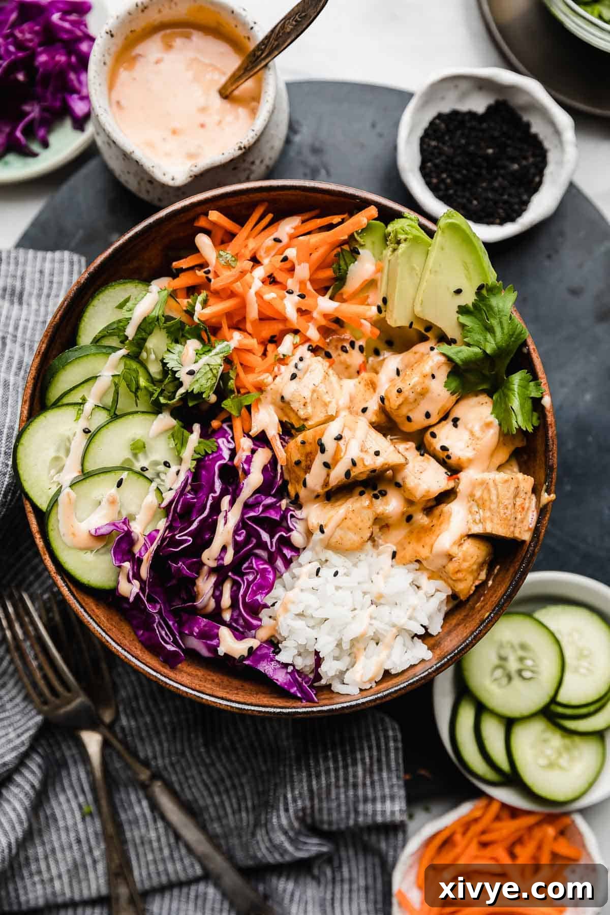 Effortless Bang Bang Chicken Bowls 10 A bang bang chicken bowl filled with white rice, bang bang chicken bites, cucumber, shredded carrots, cabbage, all on a black surface.