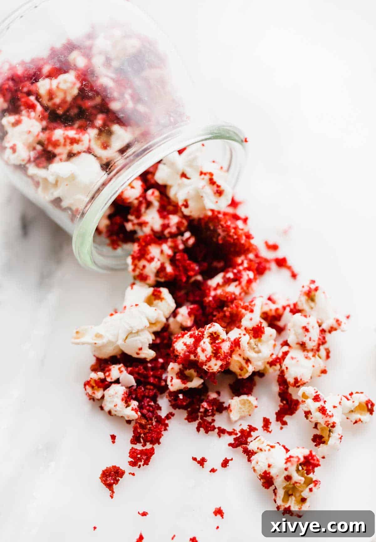 Red Velvet Popcorn spilling onto a white table from a glass cup, ready to be enjoyed.