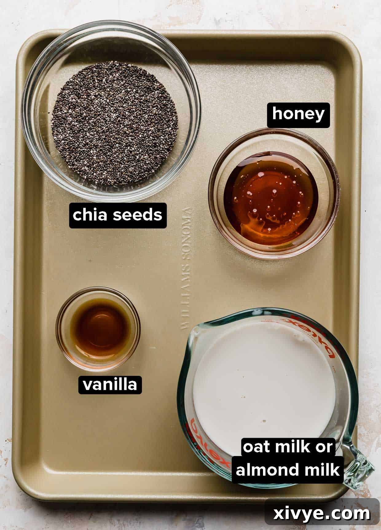 Overnight Oat Milk Chia Pudding 3 Chia Pudding with Oat Milk ingredients on a bronze baking sheet: chia seeds, vanilla, honey, and oat milk.