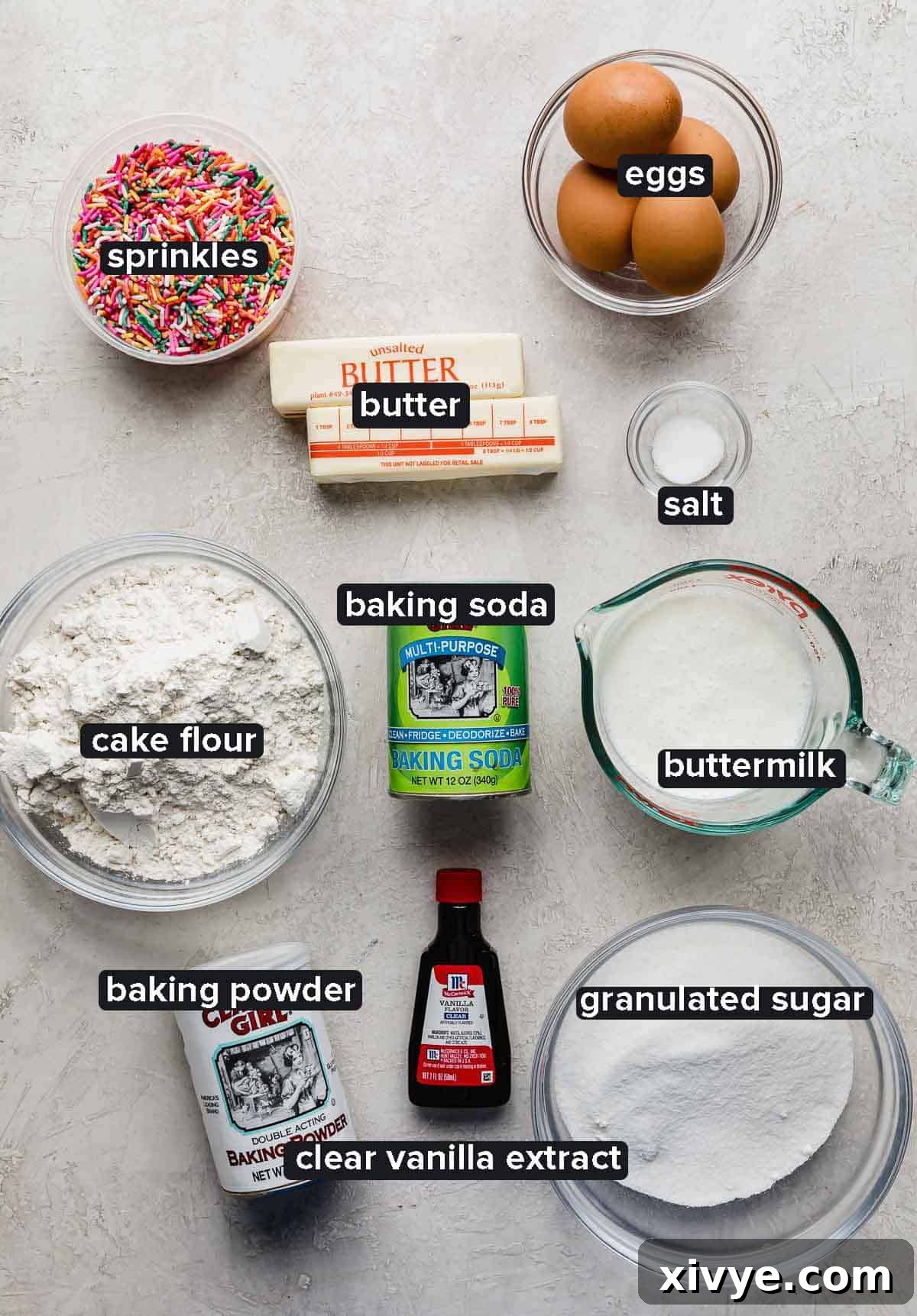 All the dry and wet ingredients for the Funfetti Cake batter, portioned into glass bowls on a light gray background, ready for mixing.