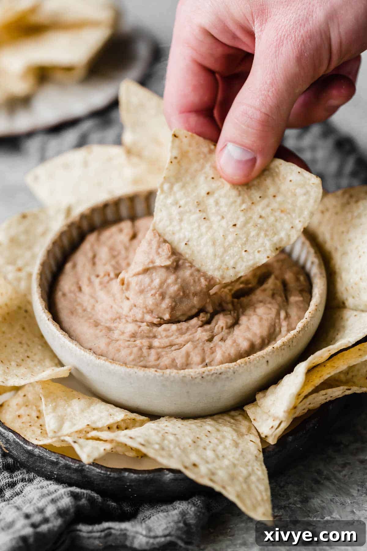Hands-Off Slow Cooker Refried Beans 7 A tortilla chip being dipped into a bowl filled with homemade refried beans.