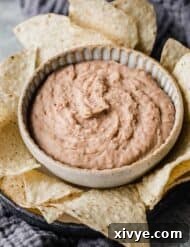 Slow Cooker Refried Beans in a bowl surrounded by tortilla chips.