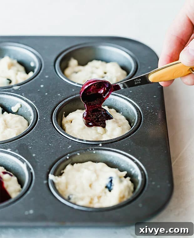 Sunrise Buttermilk Blueberry Muffins 5 A muffin tin with blueberry muffin batter, and a fresh blueberry compote being poured into each muffin tin.