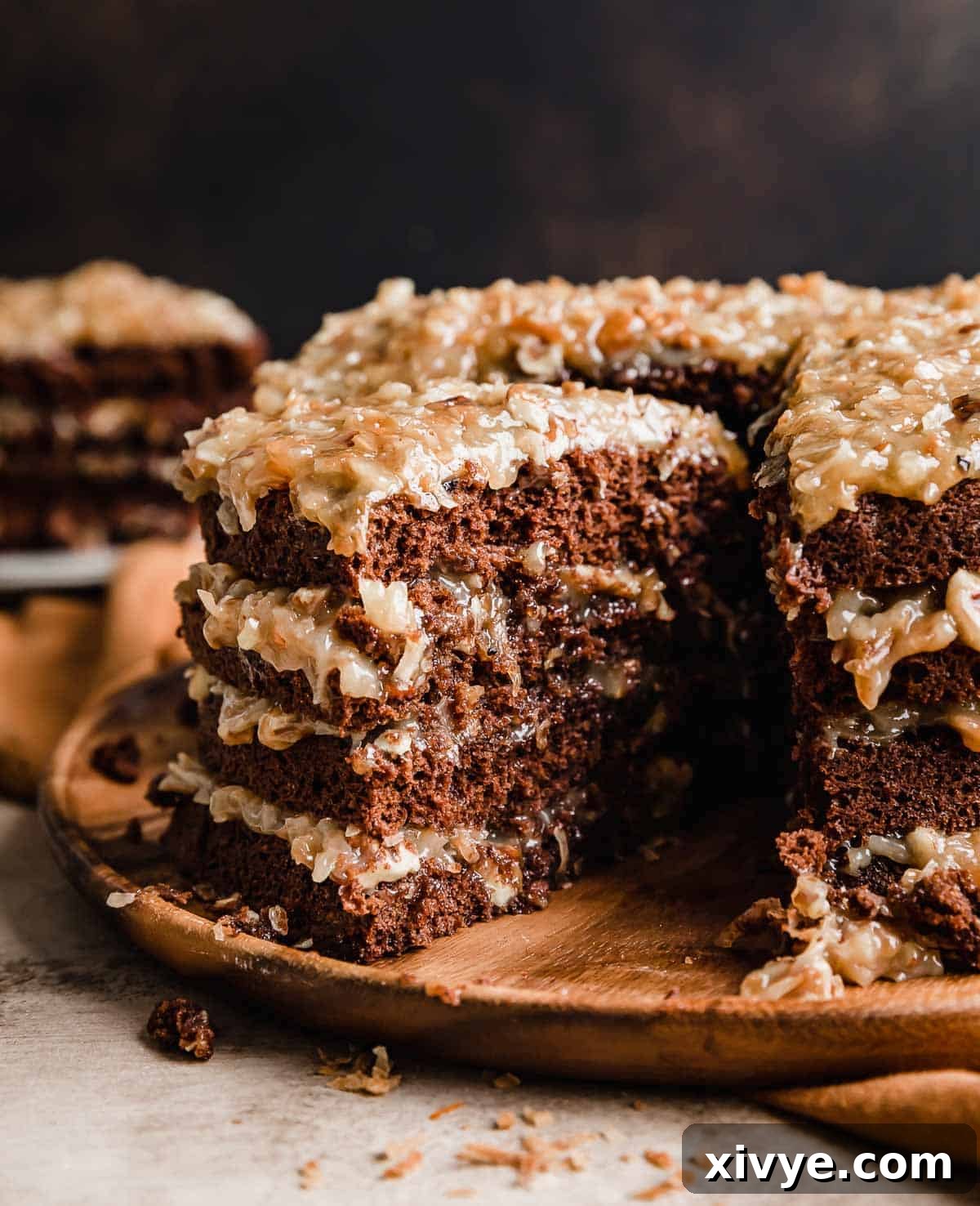 A four layer Traditional German Chocolate Cake with a slice cut from the main cake, showcasing its moist layers and rich coconut pecan frosting.