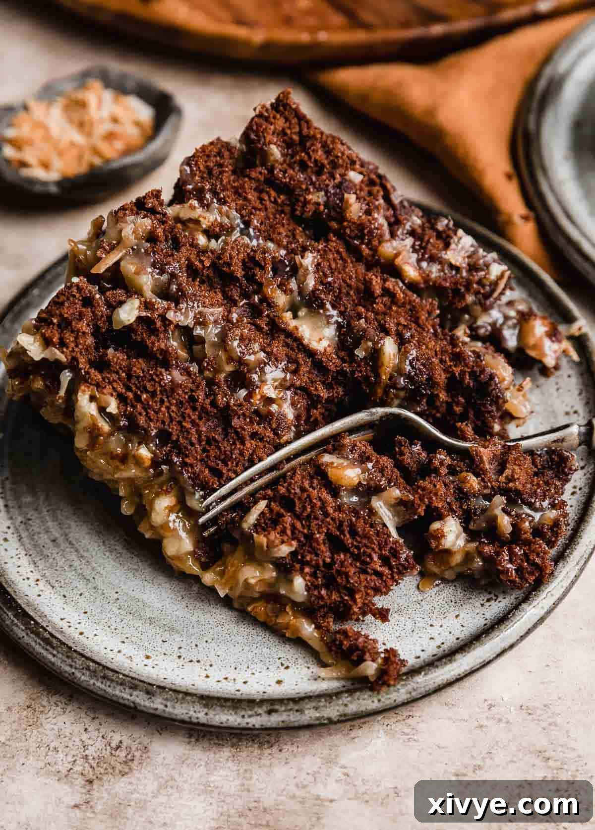 A slice of Traditional German Chocolate Cake made with sour cream, on a gray plate with a fork cutting into the cake, revealing its rich, moist texture.