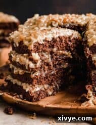 A slice of Traditional German Chocolate Cake taken from a four layer Traditional German Chocolate Cake on a wooden cake plate.