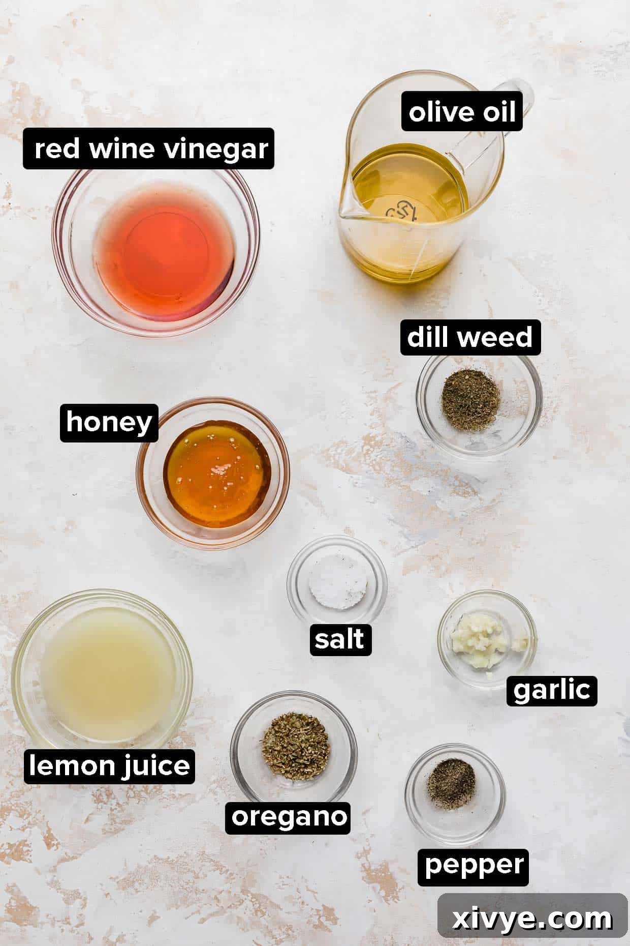 Zesty Mediterranean Pasta Salad 4 Individual glass bowls containing the distinct ingredients for the Greek pasta salad dressing: olive oil, red wine vinegar, lemon juice, honey, minced garlic, oregano, dill weed, salt, and pepper.