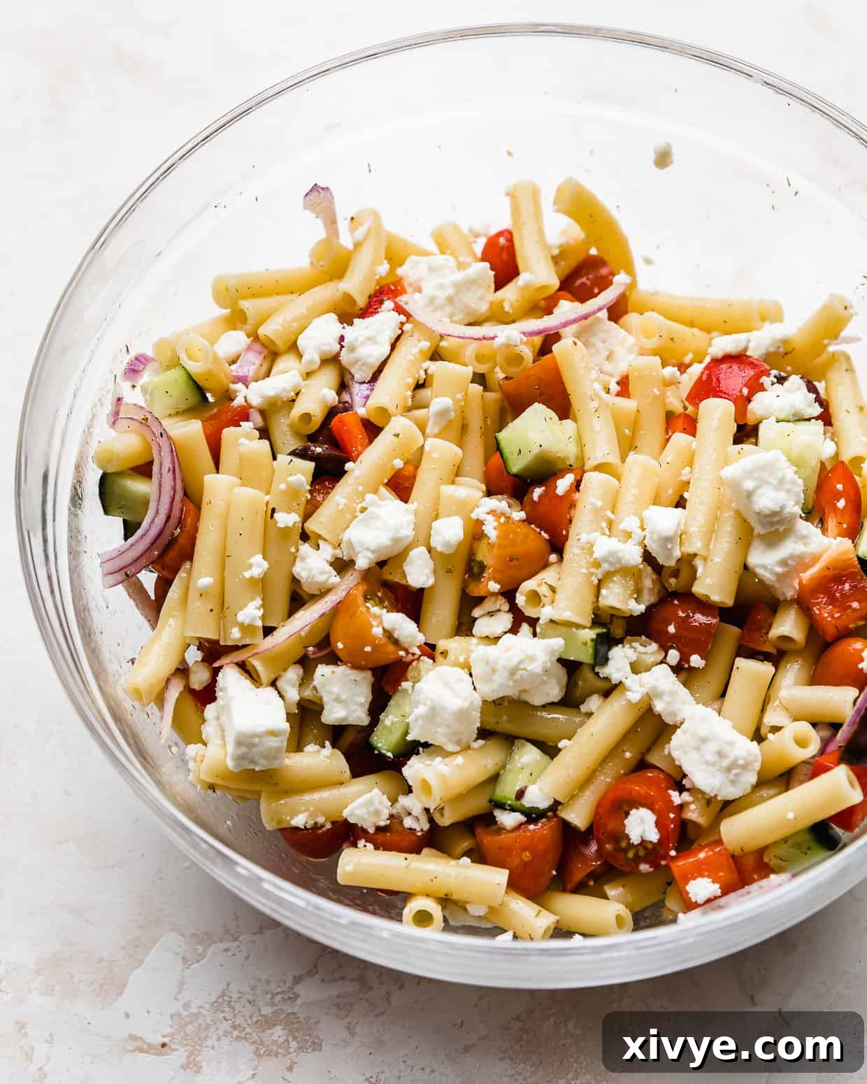 Zesty Mediterranean Pasta Salad 6 A glass bowl showcasing the finished Greek pasta salad with ziti noodles, topped generously with crumbled feta cheese.