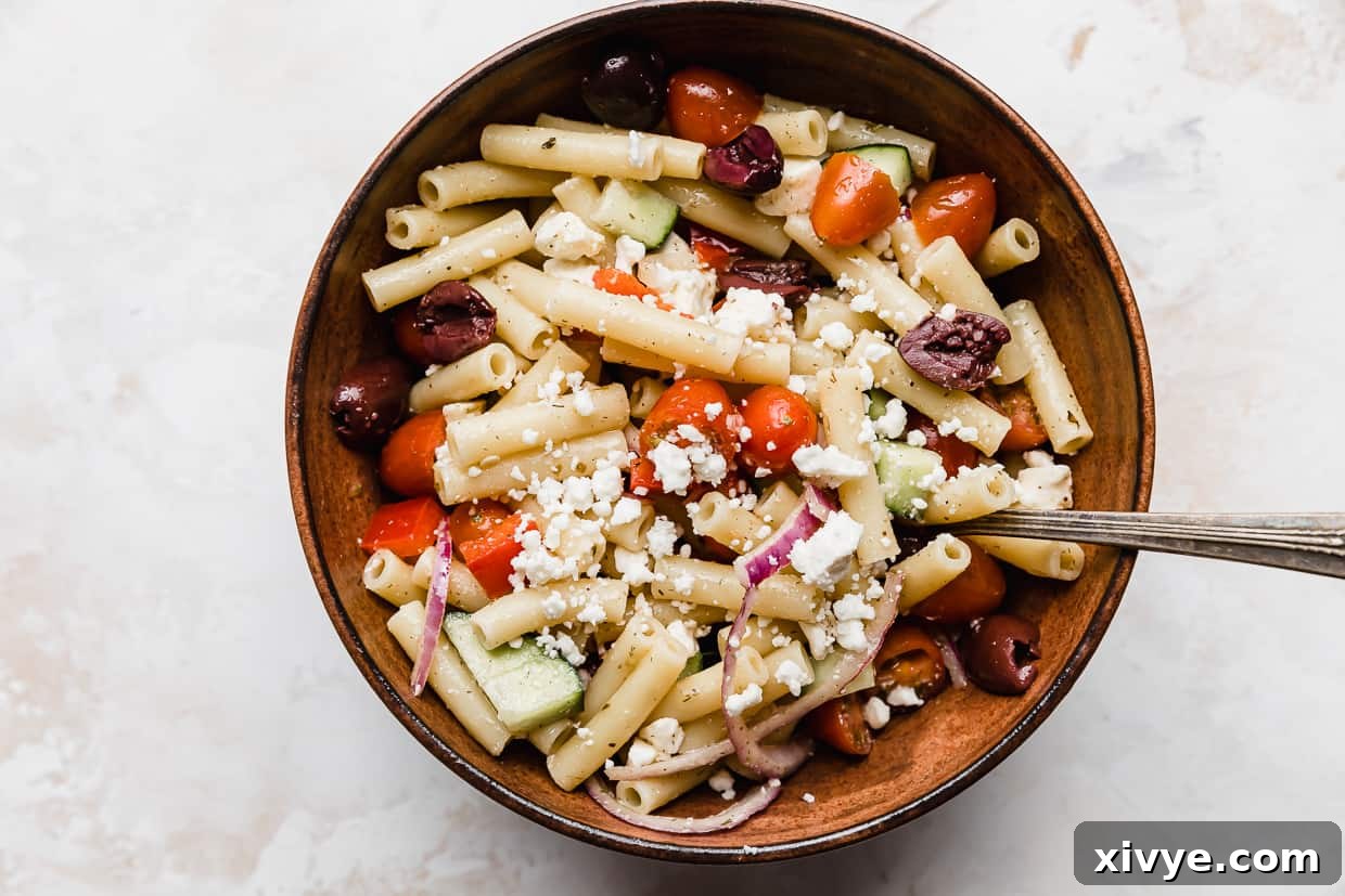 Zesty Mediterranean Pasta Salad 8 A rustic brown bowl filled to the brim with Summer Fresh Greek Pasta Salad, elegantly topped with crumbled feta cheese and a hint of fresh herbs.