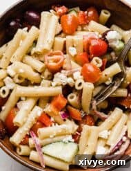 Zesty Mediterranean Pasta Salad 9 Close-up photo of a fresh Greek pasta salad with penne noodles, vibrant vegetables, and feta cheese in a rustic brown bowl.