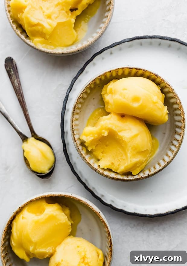 Two scoops of creamy mango sorbet in a small bowl, garnished with fresh mint.