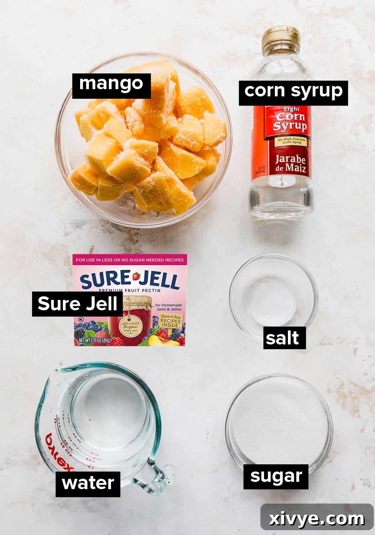Ingredients used to make mango sorbet on a white textured background, including mangoes, sugar, corn syrup, and Sure-Jell.
