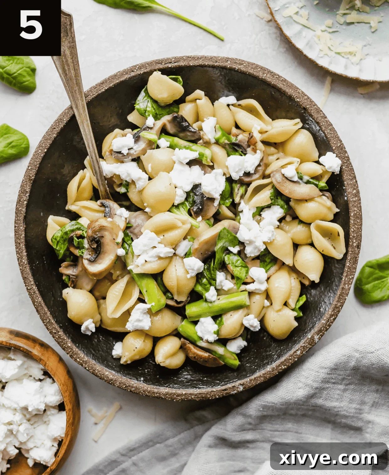 Asparagus Spinach Pasta topped with goat cheese, in a black bowl on a white background.