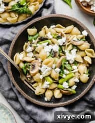 Asparagus Spinach Pasta in a black bowl on a dark gray colored linen napkin, with goat cheese garnishing the pasta.