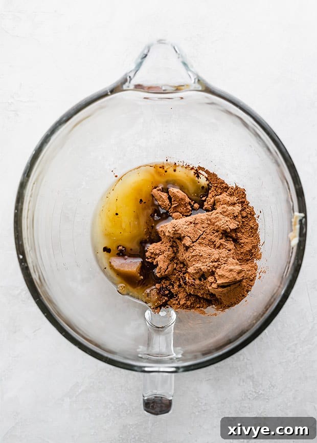 A glass bowl with cocoa powder, melted butter, sugar, and oil, ready for mixing to make brownie cookies.