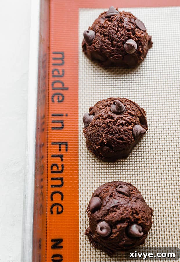Unbaked brownie cookie dough balls arranged neatly on a baking sheet lined with parchment paper, awaiting the oven.