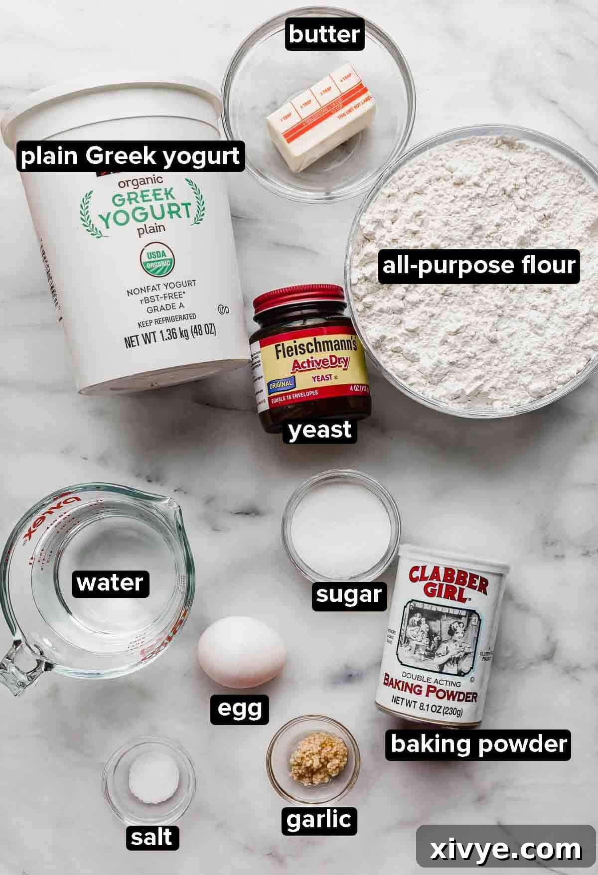 Greek Yogurt Naan Bread ingredients on a white background: yeast, flour, butter, plain greek yogurt, water, egg, garlic, and baking powder.