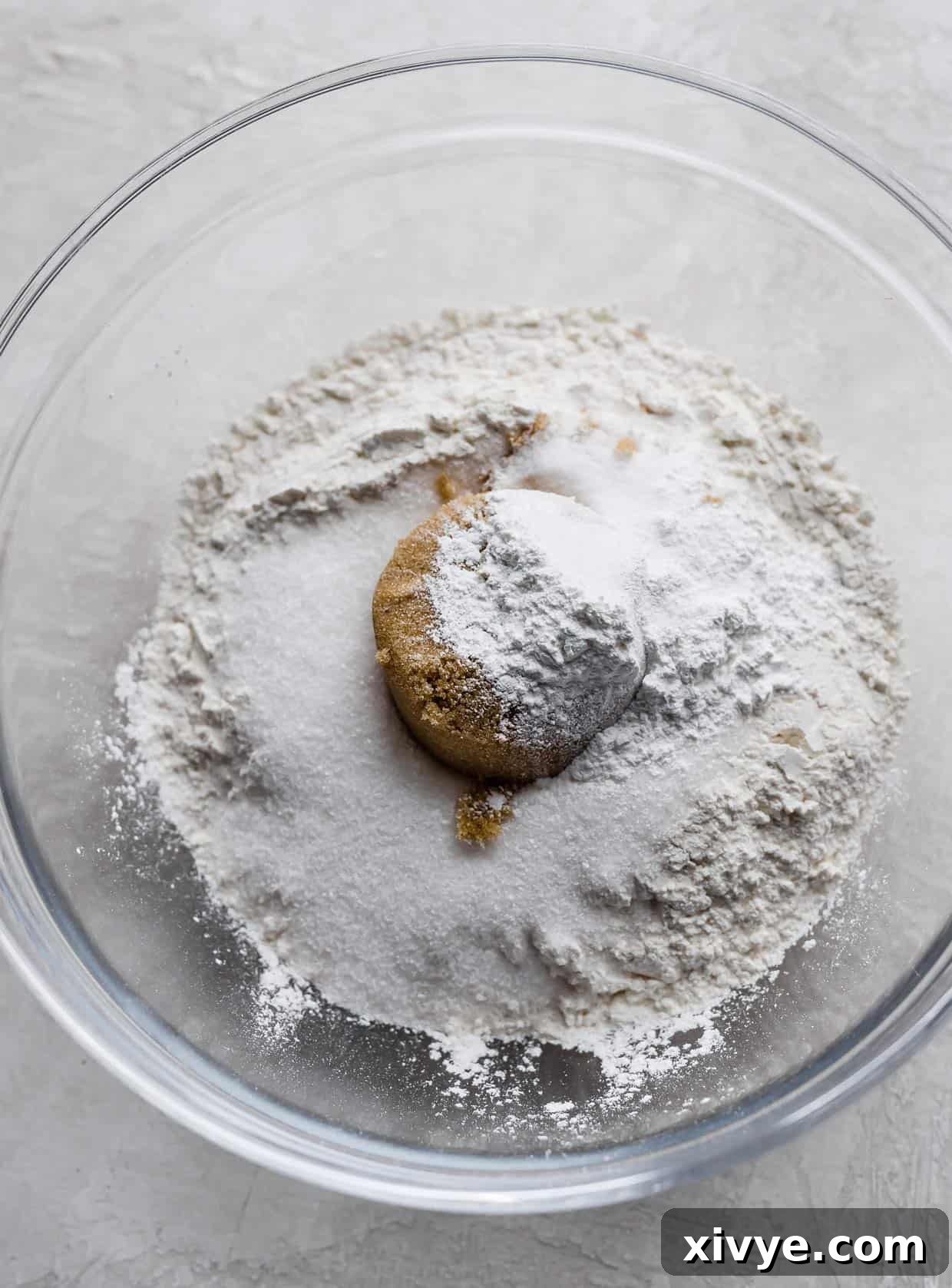 A clear glass bowl filled with white and light brown dry ingredients, including flour, granulated sugar, light brown sugar, salt, and baking powder, perfectly mixed and ready for the next step in making banana chocolate chip muffins.