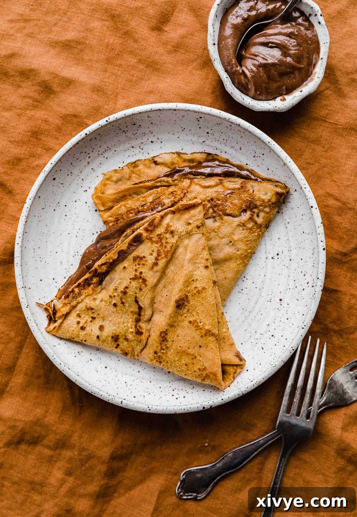 Golden Pumpkin Crepes 5 Two Nutella filled pumpkin crepes on a white plate on a burnt orange background.