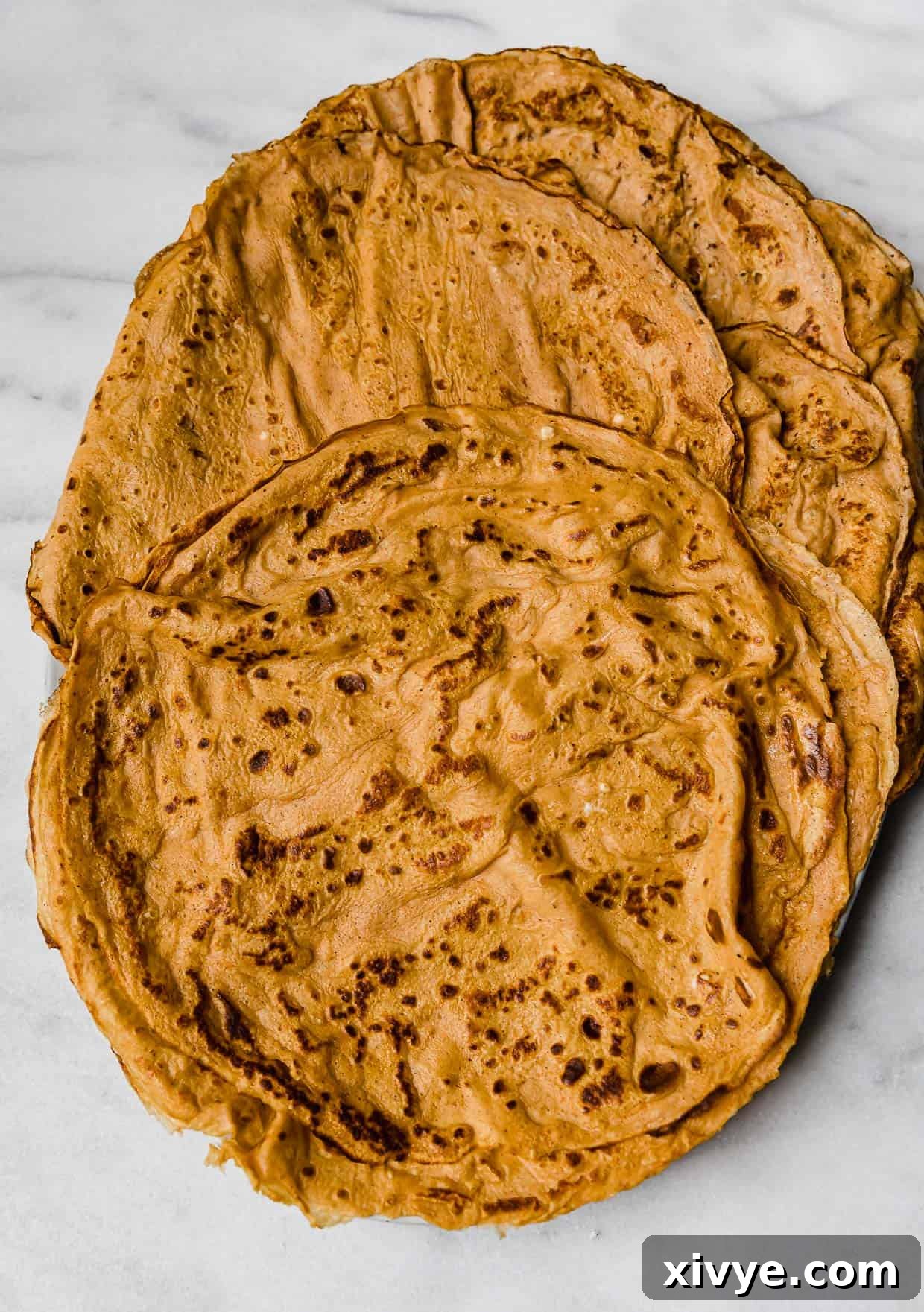 Golden Pumpkin Crepes 6 A stack of orange pumpkin crepes on a marble table.