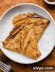 Two Nutella filled pumpkin crepes on a white plate.