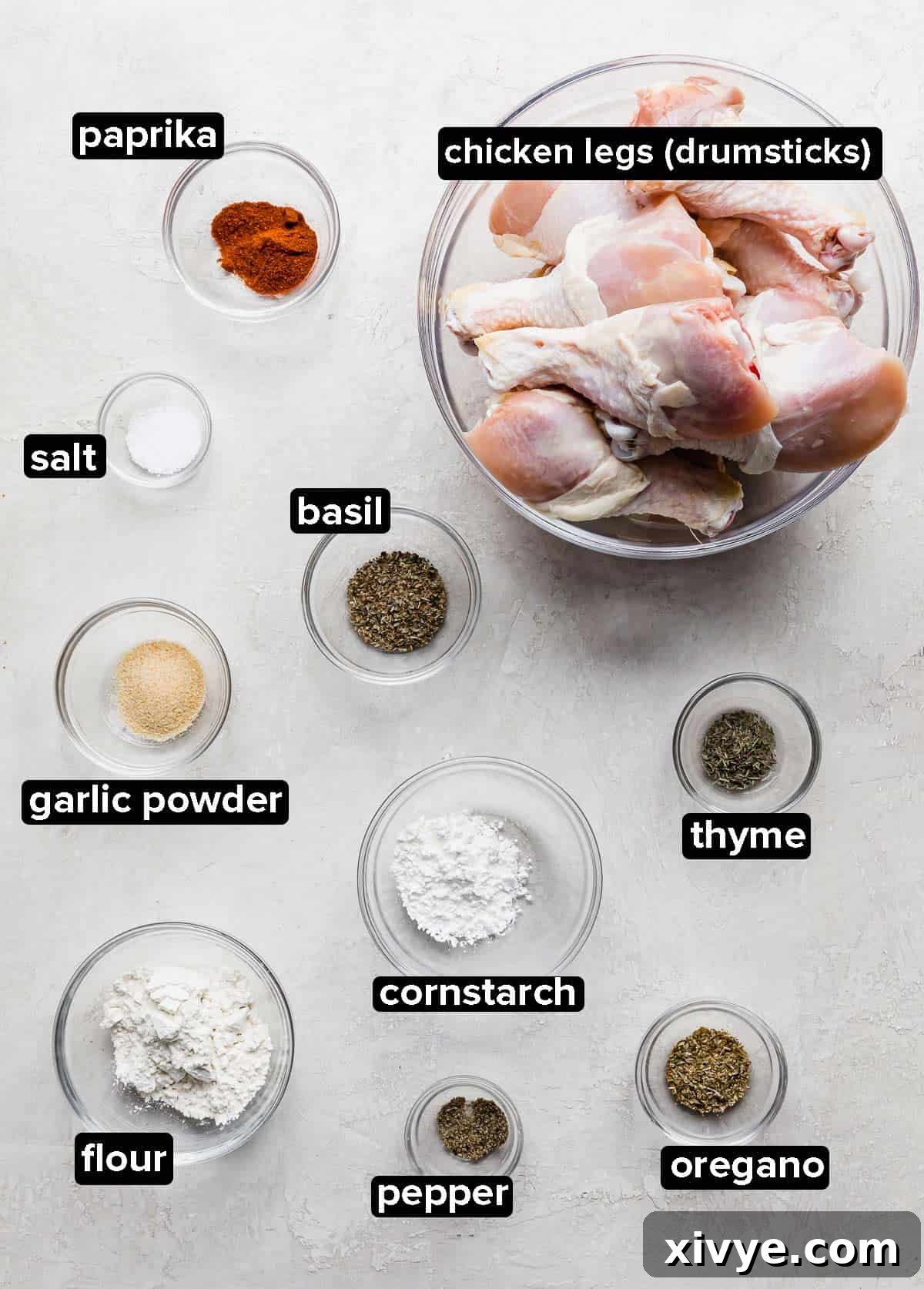 Crispy Baked Chicken Drumsticks 3 Individual glass bowls containing the raw ingredients for Oven Baked Chicken Legs, including flour, cornstarch, and various spices, arranged on a light gray background.