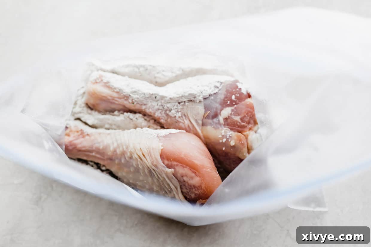 Crispy Baked Chicken Drumsticks 5 Two raw chicken legs being placed into a ziplock bag filled with seasoning mixture on a white background, demonstrating the coating process.