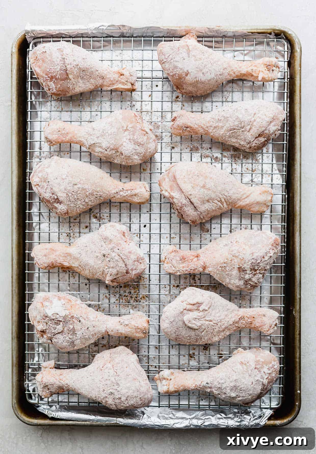 Crispy Baked Chicken Drumsticks 7 Chicken drumsticks coated in flour and spices, arranged neatly on a wire rack set over a baking sheet, ready for baking.