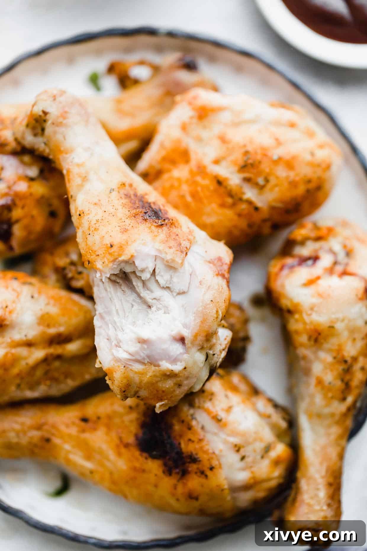 Crispy Baked Chicken Drumsticks 8 A perfectly baked, crispy Oven Baked Chicken Leg with a bite taken out, resting on a bed of other golden drumsticks on a white plate, showcasing its juicy interior.