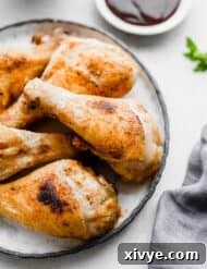 Crispy Oven Baked Chicken Legs on a white plate with barbecue sauce in a small bowl in the background.